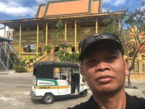 Meet Bunna at a Historic Phnom Penh Temple Bunna standing beside his tuk tuk in front of a Buddhist temple in Phnom Penh