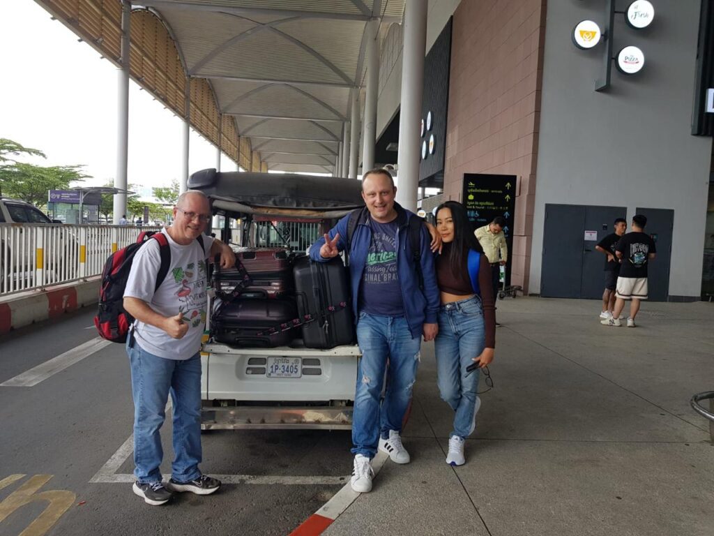 Local guide Bunna assisting two travelers with their luggage next to a tuk-tuk outside Phnom Penh International Airport.
