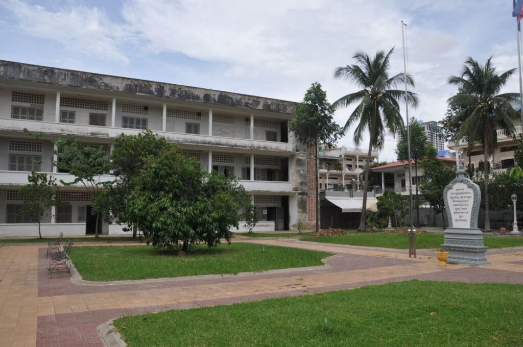 Exterior view of Tuol Sleng Genocide Museum (S-21 Prison) in Phnom Penh, Cambodia, with green lawn and palm trees.